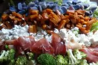 Слоеный овощной салат с прошутто и фетой на доске